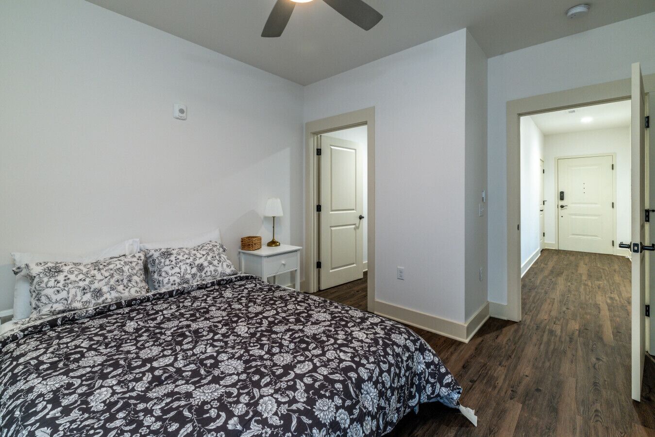 A bedroom with a bed, nightstand, lamp, and a door leading to another room.