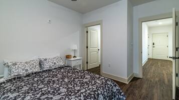 A bedroom with a bed, nightstand, lamp, and a door leading to another room.