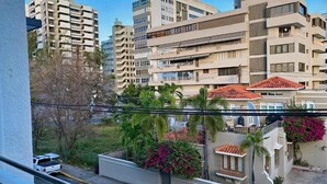 A residential building with multiple balconies, a parking area, and a view of surrounding high-rise buildings.
