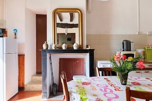 A kitchen with a wooden door, a white refrigerator, a black stove, a microwave, and a table with a floral tablecloth.