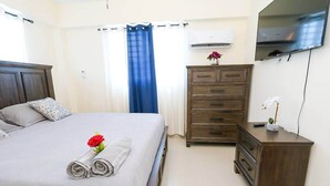 A hotel room with a bed, a dresser, a nightstand, an air conditioner, and a TV.