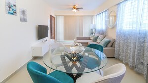 A modern living room with a glass dining table, teal chairs, a beige sofa, and a ceiling fan. - Beautiful 2Bd/2bath apt W. AC, Garage  & roof top (San Cristobal)