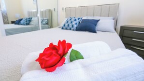 A neatly made bed with a single red rose and a white towel, a wooden headboard, and a nightstand with a drawer. - Beautiful 2Bd/2bath apt W. AC, Garage  & roof top (San Cristobal)