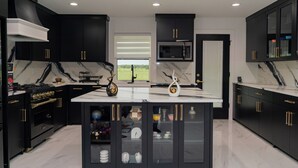 A modern kitchen with black cabinets, a marble countertop, and gold handles. - Peaceful Farmhouse Retreat in Van Alstyne (Van Alstyne)