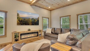 Ein gemütliches Wohnzimmer mit Kamin, einem großen an der Wand befestigten Fernseher und einer komfortablen Sitzecke mit Sofa und Sesseln.