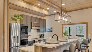 Eine moderne Küche mit Edelstahlgeräten, einer Holztheke mit Barhocker und Blick ins Freie durch große Fenster.
