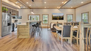 Eine moderne Küche mit Holzboden, einer zentralen Kochinsel, Barhocker und einem Essbereich mit Holztisch und Stühlen.