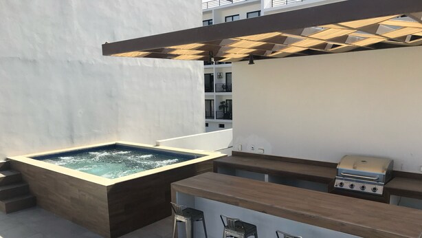 A rooftop bar with a hot tub, bar stools, and a grill.