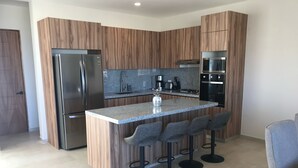 A modern kitchen with a central island, bar stools, stainless steel appliances, and wooden cabinetry.