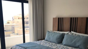 A bedroom with a large bed, a wooden headboard, and a view of buildings through a window.