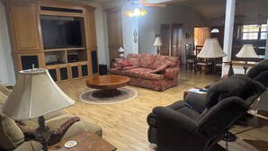 Una sala de estar con piso de madera, un sofá, una silla, una mesa de centro y un televisor.