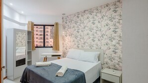 Een slaapkamer met een bed, een kledingkast, een bureau en een raam met gordijnen.