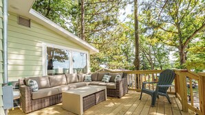 A wooden deck with a sofa and chairs, surrounded by trees. - Lakefront | Sauna, Kayaks, Fire Pit, & Huge Deck (Mecosta)