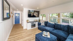 A living room with a blue sofa, a coffee table, a TV mounted on the wall, and a fireplace. - Lakefront | Sauna, Kayaks, Fire Pit, & Huge Deck (Mecosta)