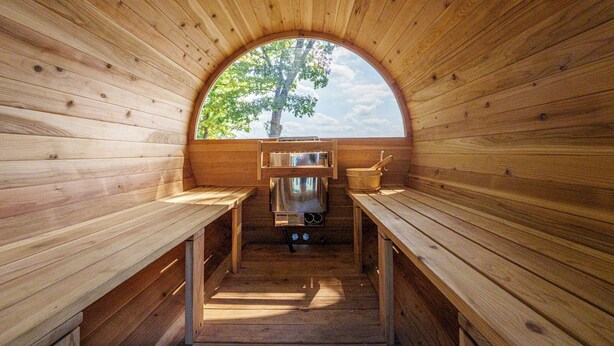 A wooden sauna with benches and a sauna table, a window with a tree view, and a sauna heater. - Lakefront | Sauna, Kayaks, Fire Pit, & Huge Deck (Mecosta)