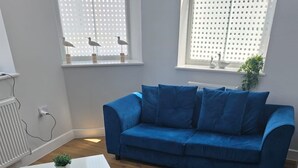 Een woonkamer met een blauwe bank, een witte salontafel en een kleurrijk abstract tapijt.