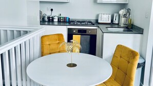 Een moderne keuken met witte kasten, een gasfornuis en een spoelbak. Er staat een ronde witte tafel met vier stoelen in mosterdgeel.