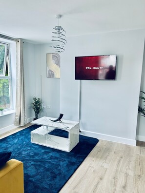 A modern living room with a mounted TV, a marble coffee table, a blue rug, and a wooden floor.