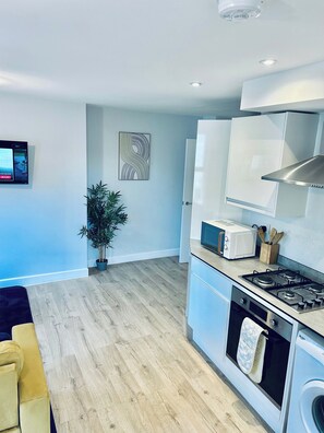 A modern kitchen with a built-in oven, microwave, and gas stove. There is a potted plant and a wall-mounted TV.