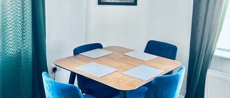 Ein Essbereich mit einem runden Tisch, vier blauen Stühlen und einem gerahmten Bild an der Wand.