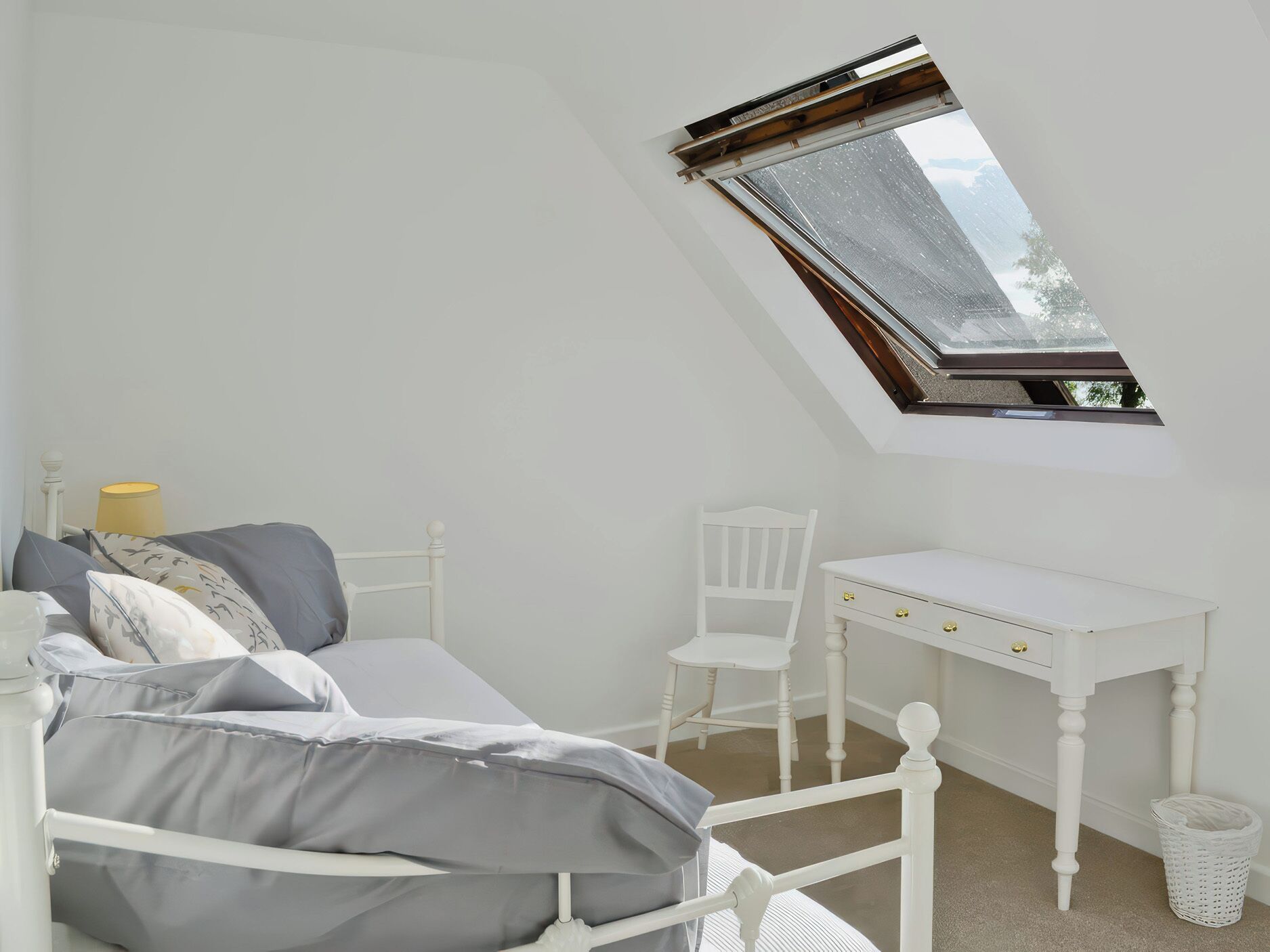 Een slaapkamer met een schuine balkenkap, een bed, een bureau en een stoel.
