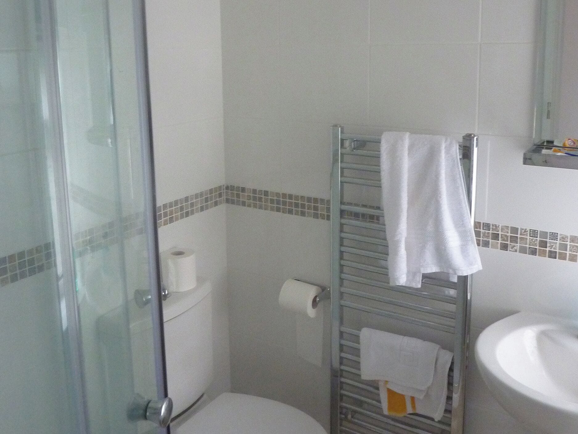 A bathroom with a glass shower enclosure, a toilet, a towel rack with towels, and a sink.