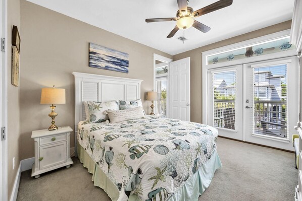 A bedroom with a bed, nightstands, a ceiling fan, and a view through the door.