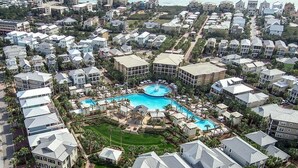 Vista aérea de un complejo turístico con varias edificaciones, una piscina central y vegetación circundante.