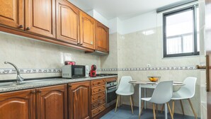 A kitchen with wooden cabinets, a microwave, a coffee maker, and a dining area with two chairs and a table. - Pena View Apartment by Atlantic Holiday (Funchal)