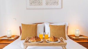 A neatly made bed with two pillows, a tray with croissants and orange juice, and two lamps on nightstands. - Pena View Apartment by Atlantic Holiday (Funchal)