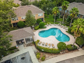 Vista aérea de una zona residencial con piscina rodeada de sillones de descanso y palmeras.