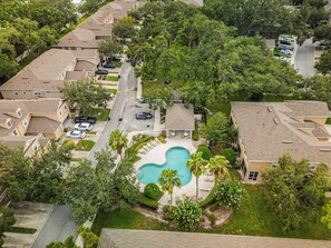 Vista aérea de un área residencial con piscina rodeada de palmeras y algunas casas.