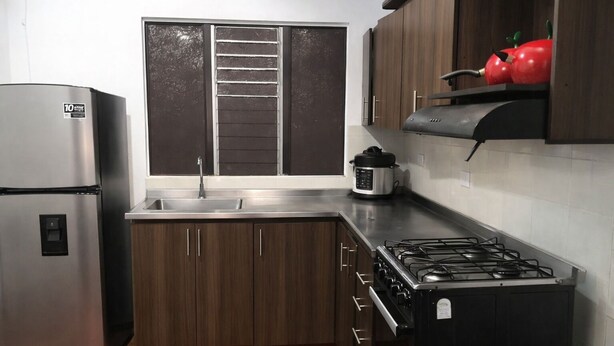A kitchen with a stainless steel refrigerator, a gas stove, wooden cabinets, a window with blinds, and a red apple on the shelf. - Two rooms AREAS by QuBeLab (Bello)