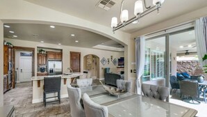 A spacious living area with a large glass dining table, comfortable seating, and a kitchen in the background. - Havasu Duke - Pool, Spa, Basketball, Central (Lake Havasu City)