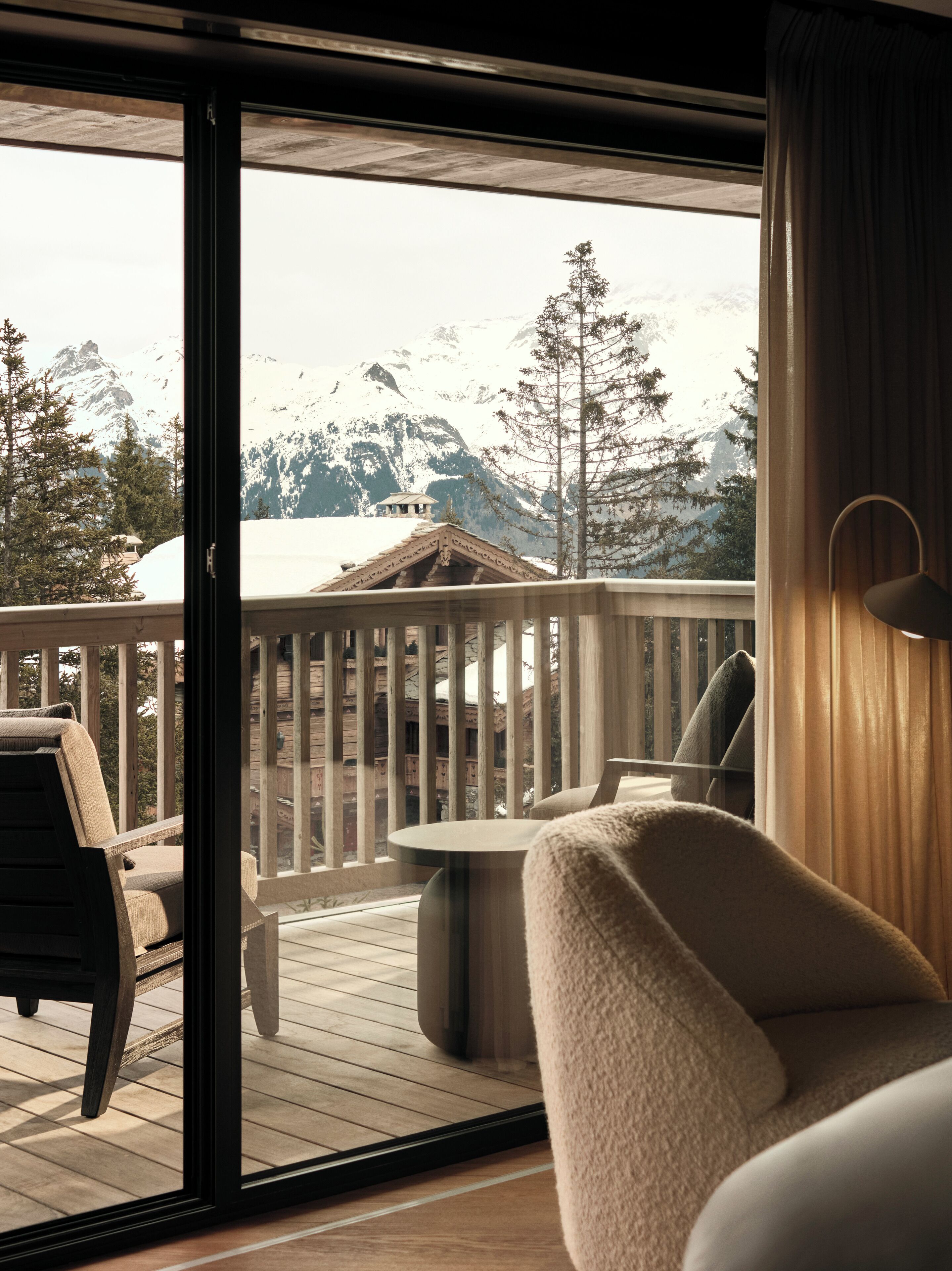 A balcony with a wooden deck, a chair, a table, and a view of snow-covered mountains.