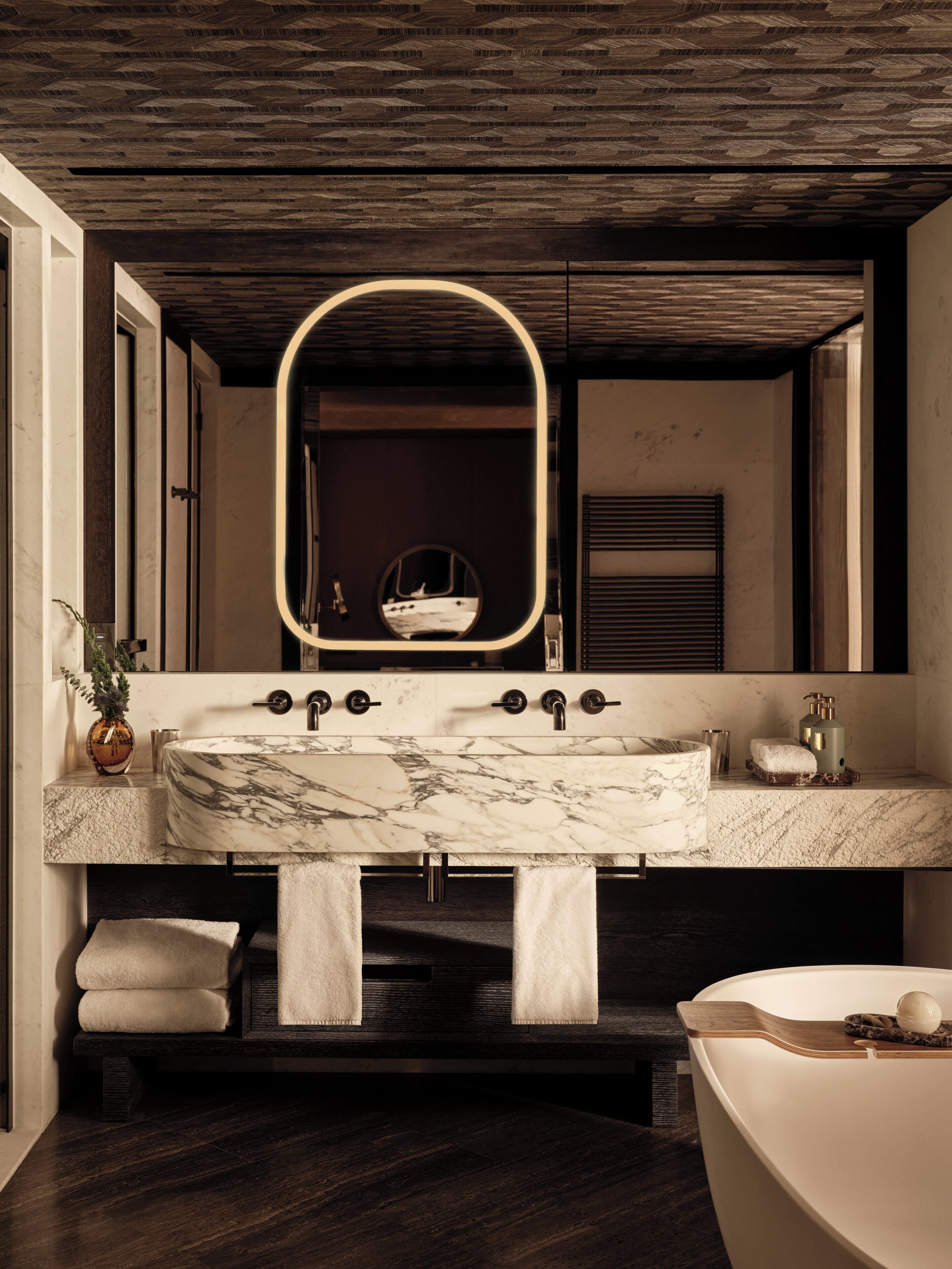 A modern bathroom with a marble sink, a large mirror, and a bathtub.