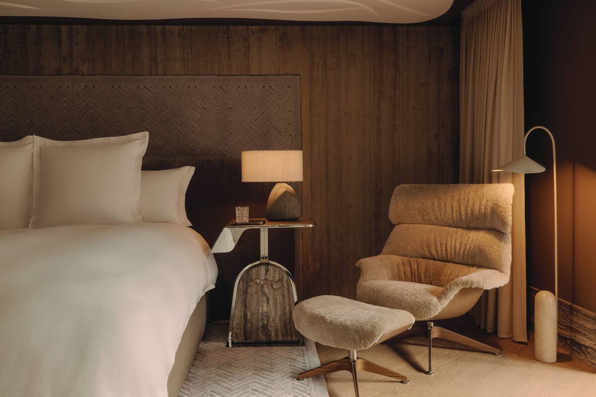 A hotel room with a large bed, a chair, a desk with a lamp, and a nightstand.