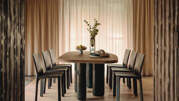 A round dining table with six chairs, a vase with flowers, and a bowl of fruit on the table.