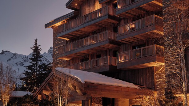 Un edificio de varios pisos con balcones, fachada de madera y suelo cubierto de nieve.