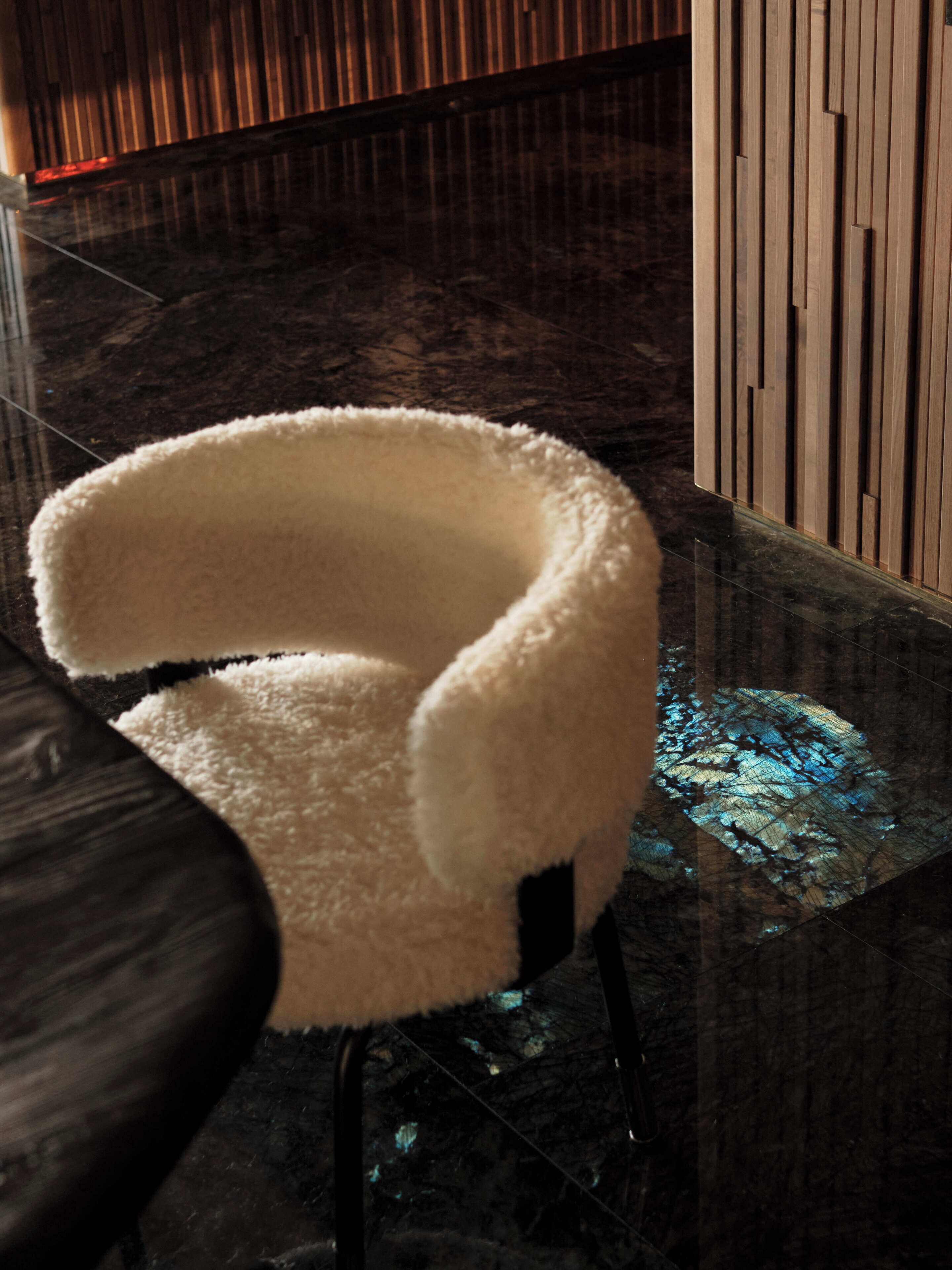 A white, fluffy chair with a curved backrest, positioned on a glass table with a reflective surface.