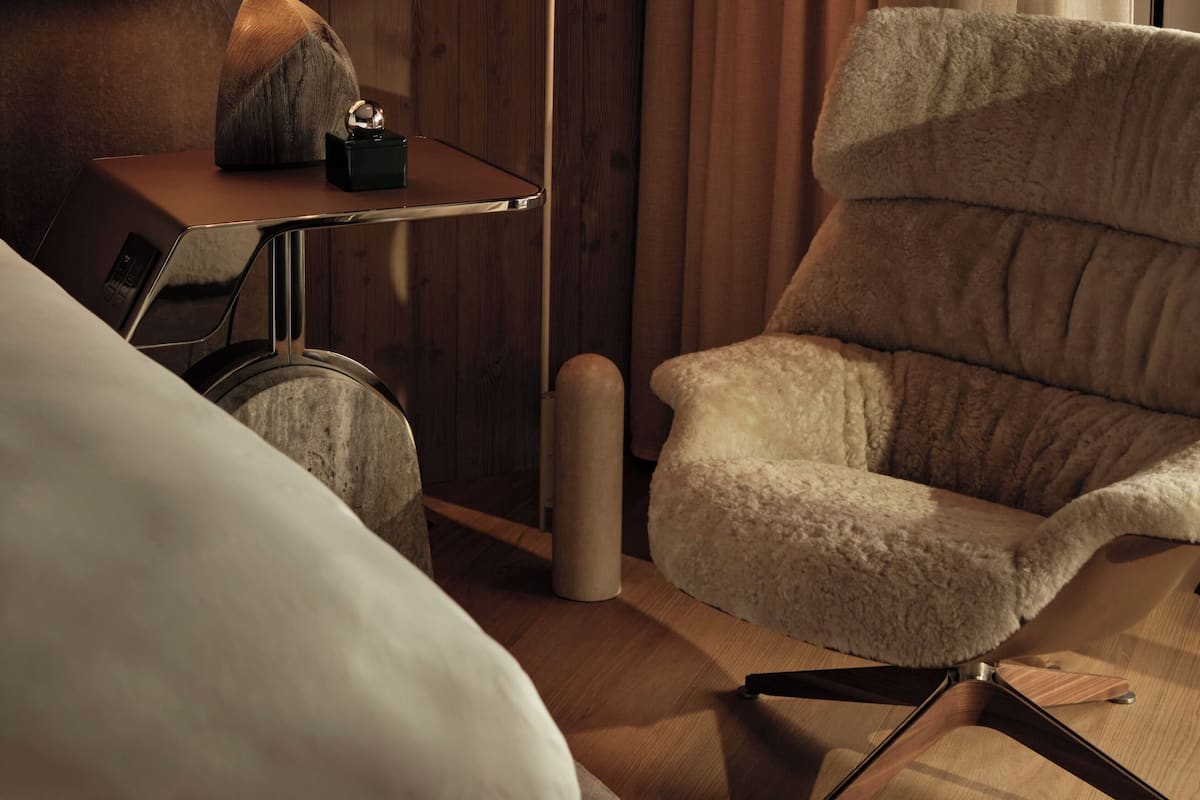 A hotel room with a bed, a desk with a lamp, a chair, and a wooden wall.
