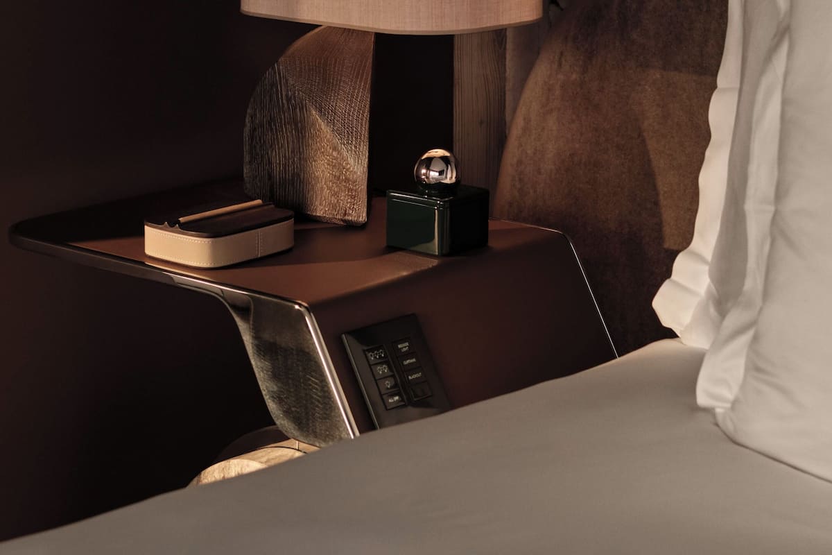 A neatly arranged hotel room with a bedside table, a lamp, a clock, and a bed with a pillow.