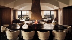 Un salón amplio con una mesa redonda grande, sillones cómodos, una chimenea y vistas a montañas nevadas a través de amplios ventanales.