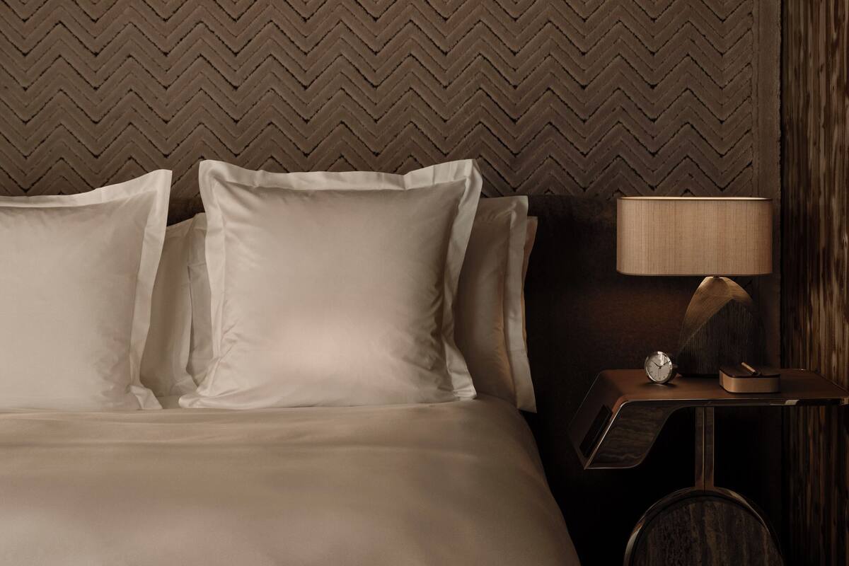 A hotel room with a large bed, a wooden headboard, a nightstand with a lamp, and a clock.