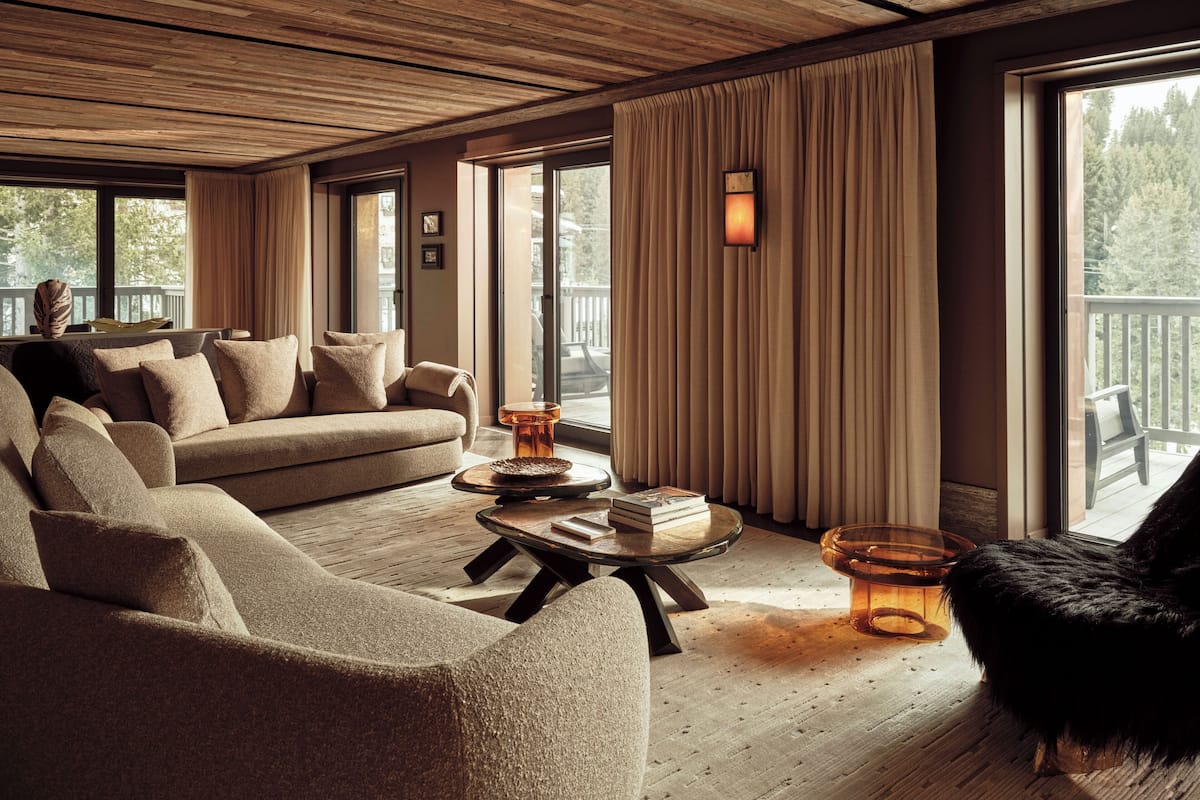 A cozy living room with a wooden ceiling, large windows, a sofa, a coffee table, and a fireplace.