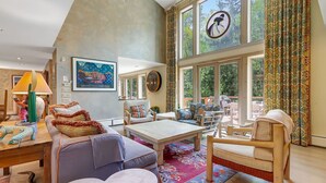 A spacious living room with a high ceiling, large windows, and a cozy seating area.