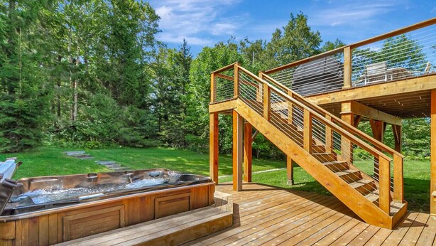 A wooden deck with a hot tub and a staircase leading to a covered area.