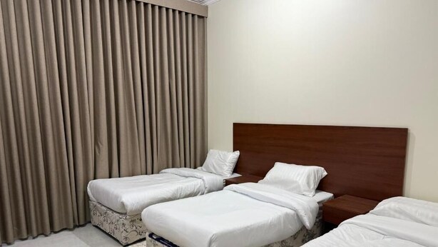 A hotel room with two single beds, a large window with curtains, and a patterned rug. - Saba Munawara Al Masi (Madinah)