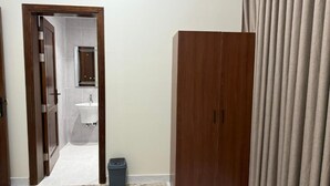 A room with a wooden wardrobe, a door leading to a bathroom, and a curtain on the right. - Saba Munawara Al Masi (Madinah)