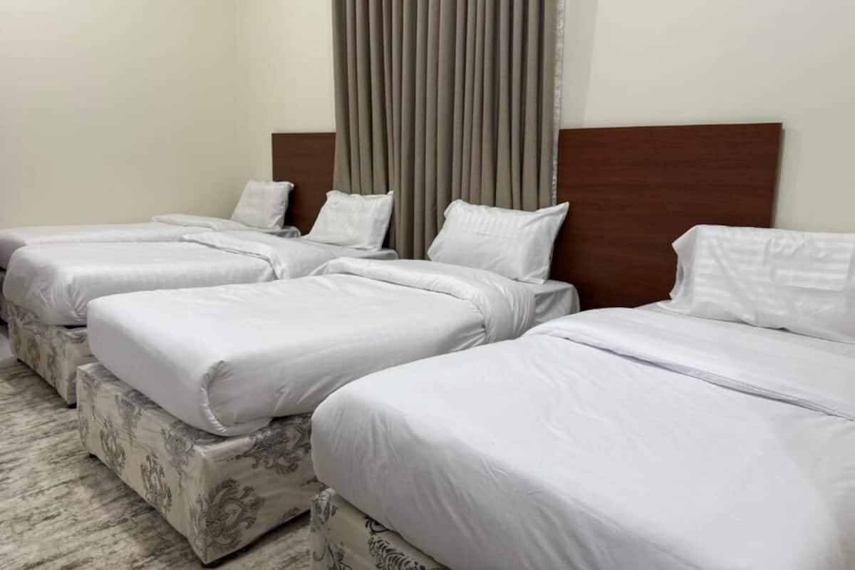 A hotel room with three single beds, each with white bedding and a wooden headboard.